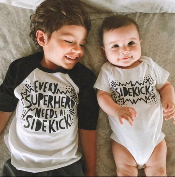 Cute Pregnancy Announcement Shirts for Siblings that say Every Superhero Needs a Sidekick for big sibling and a onesie that says Sidekick for baby