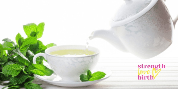 A white teapot pouring a pale liquid that I'm imagining is green tea with mint as a bunch of fresh mint sits near the cup and saucer. Mint green tea is another excellent beverage for early pregnancy.