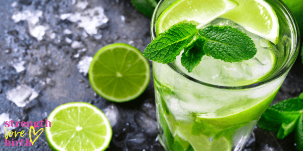 A lovely mojito mocktail in a clear glass surrounded by fresh limes and mint and cracked ice. A fun drink to enjoy during the first trimester of pregnancy.